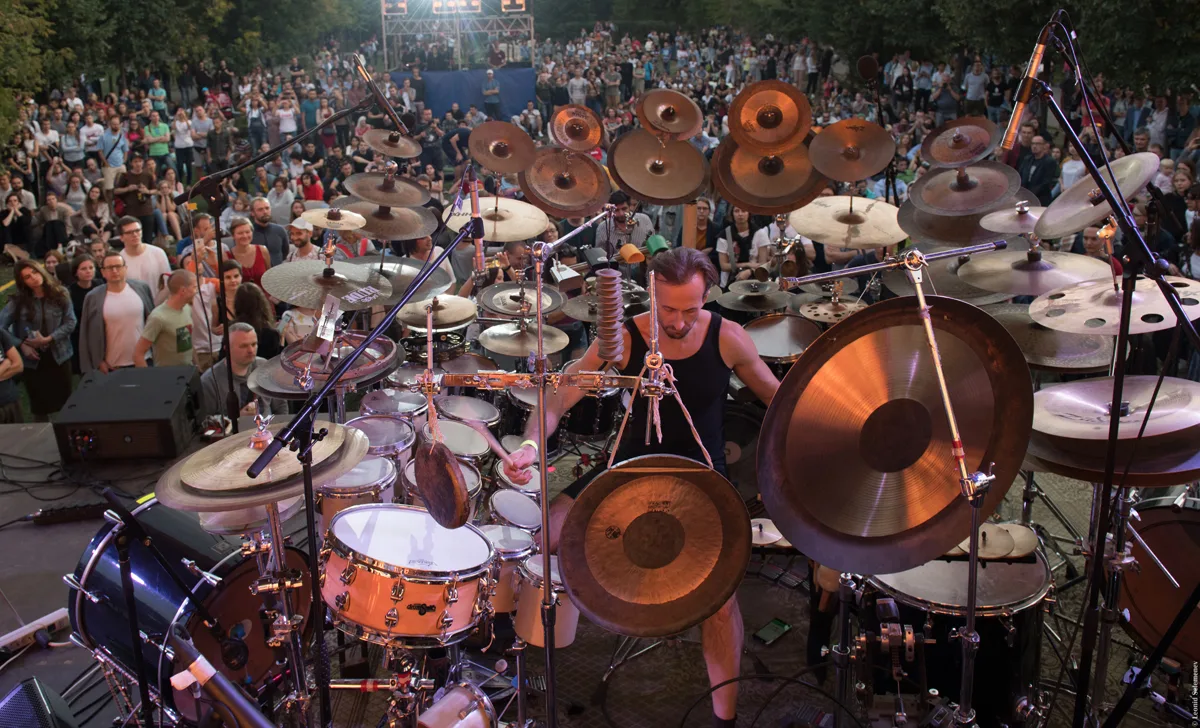 A drummer performing behind a drum kit in front of an outdoor audience